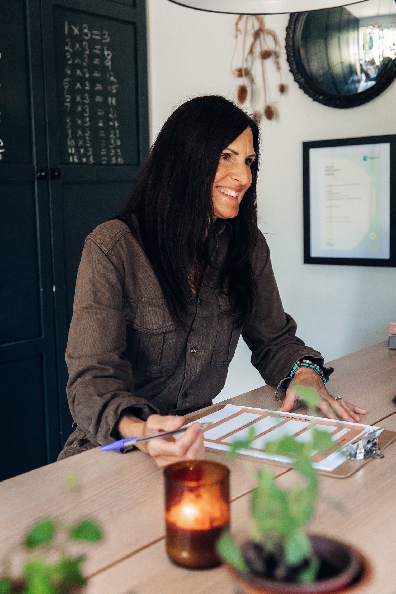 Woman sitting at a table with a clipboard and pen, smiling.