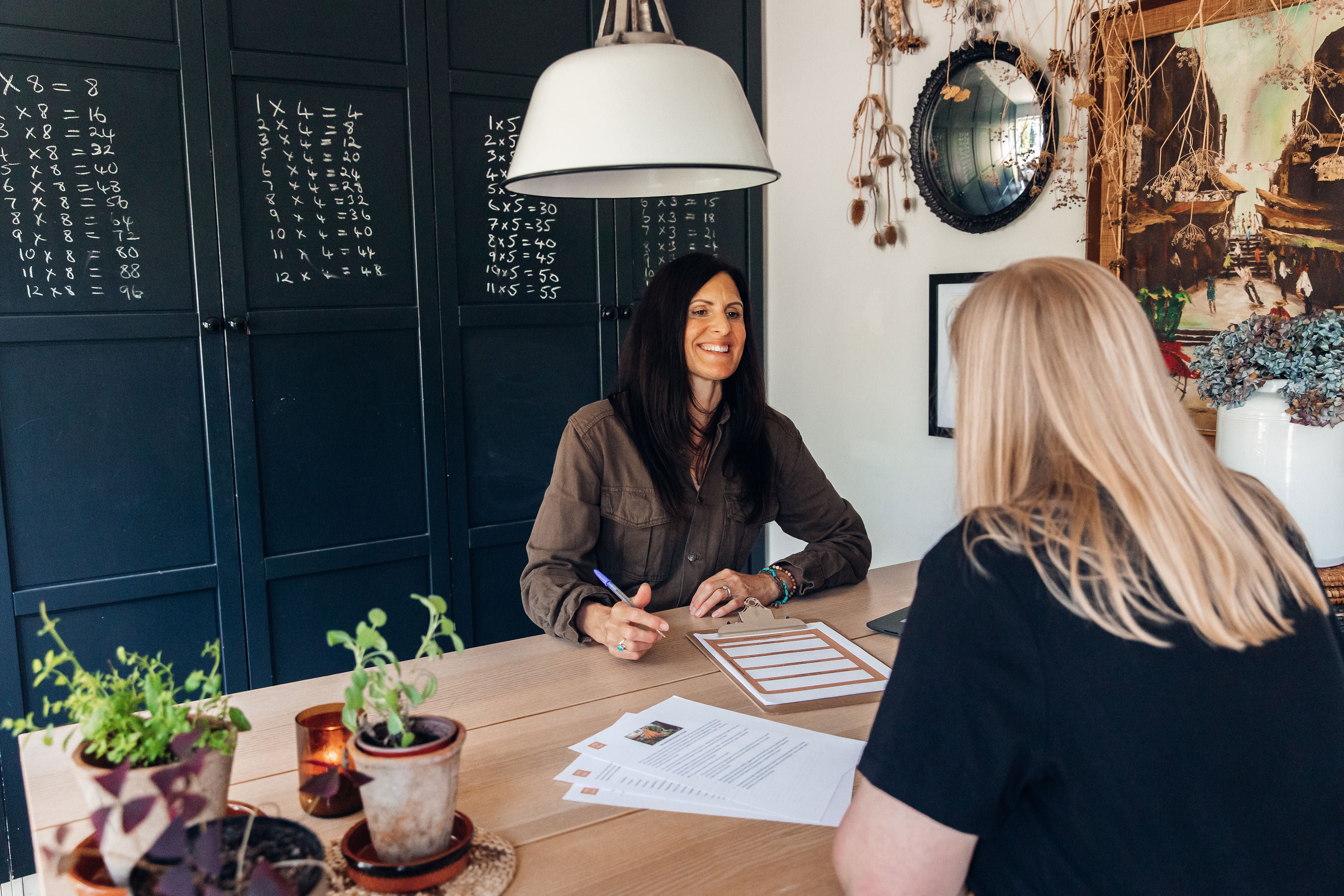 Two women sitting at a table in a room with decorative elements and plants.