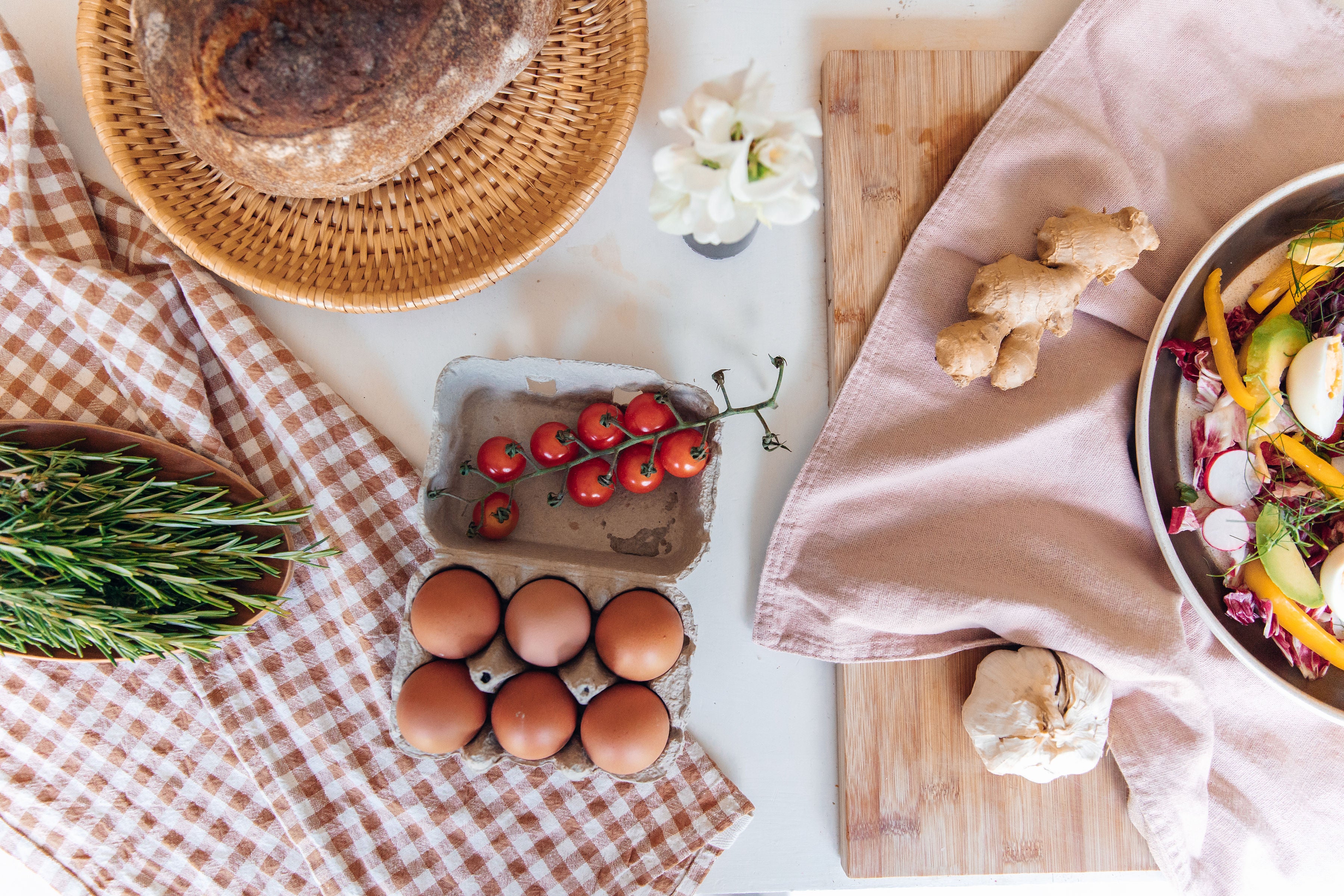 Table setting with eggs, tomatoes, bread, and vegetables on a checkered tablecloth.